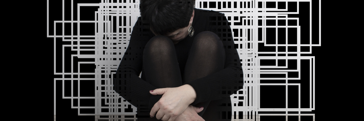 Sad woman sitting on floor with geometric art behind her.