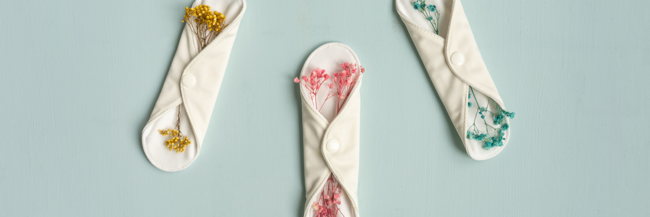 How My Hysterectomy Changed My Life Reusable eco natural pad. White feminine washable, healthy and eco friendly pads from cotton and polyester. Blue background, Zero waste lifestyle. Dry multi-colored flowers as decoration.