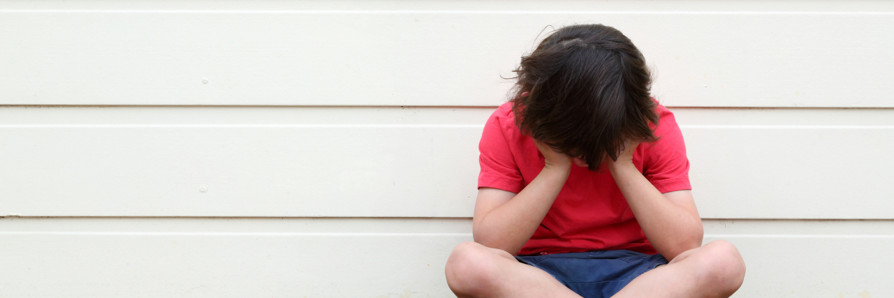 Bullying Can Lead to Self-Imposed Social Isolation for Autistic People Sad boy with head in his hands.