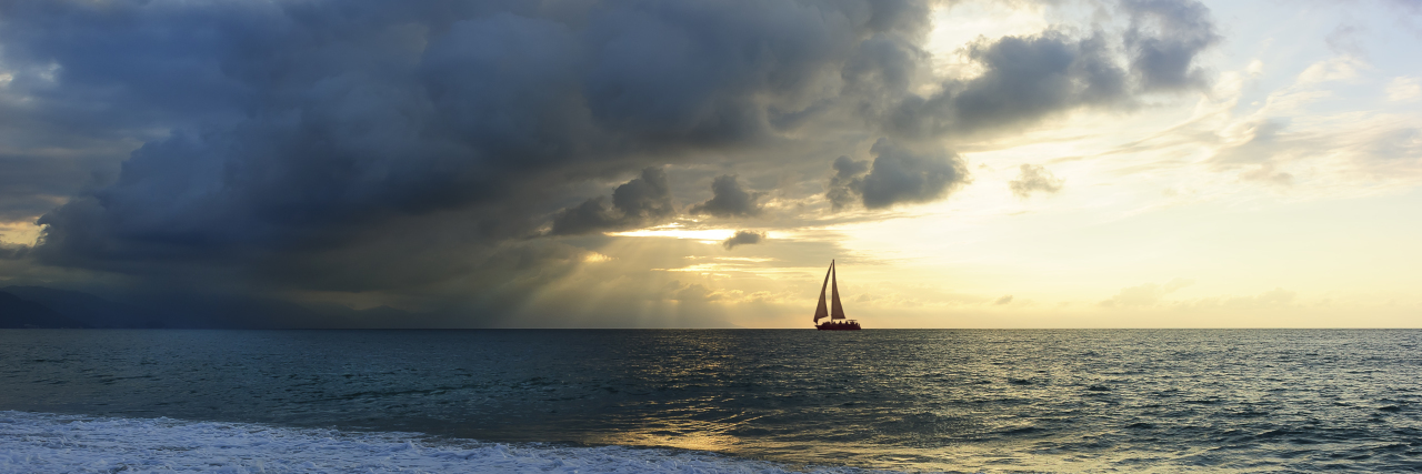 Sailboat silhouette in a burst of sun beams shooting out through the clouds.