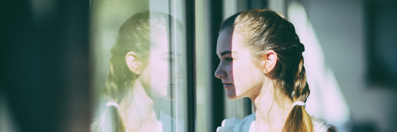 How 'Forced Disclosure' Harms Disabled People Young woman looking out window.