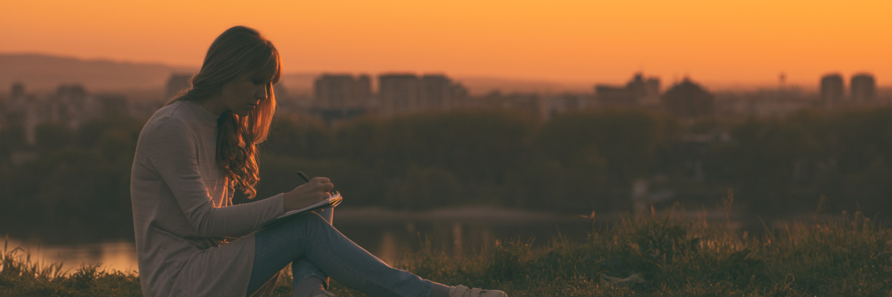 How Creative Writing Has Helped My Mental Health A young woman sitting by a lake at sunset writing in a journal