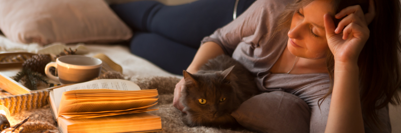 Life Lessons I've Learned From Being at Home Due to Chronic Illness Young woman with a cat in bed at home.