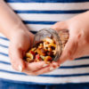 photo of a person's hands pouring dried fruit and nuts from a glass jar