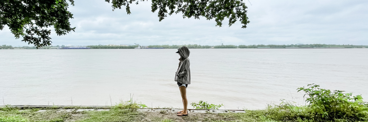Do You Gaslight Your Own Chronic Pain Experience? Woman standing alone where the forest meets the beach.