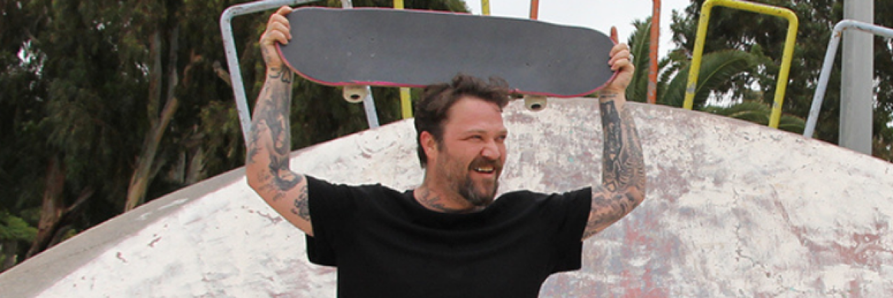 photo of Bam Margera in 2017 with a skateboard held over his head