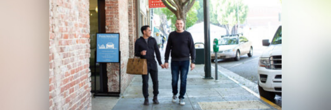 Author, a young white man and his partner walking hand-in-hand down the street, smiling
