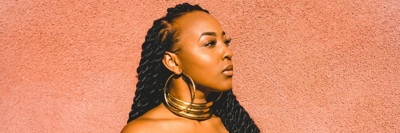 9 Tips for Supporting Someone With Chronic Mental Illness a Black woman with hoop earrings standing outside looking away contemplatively