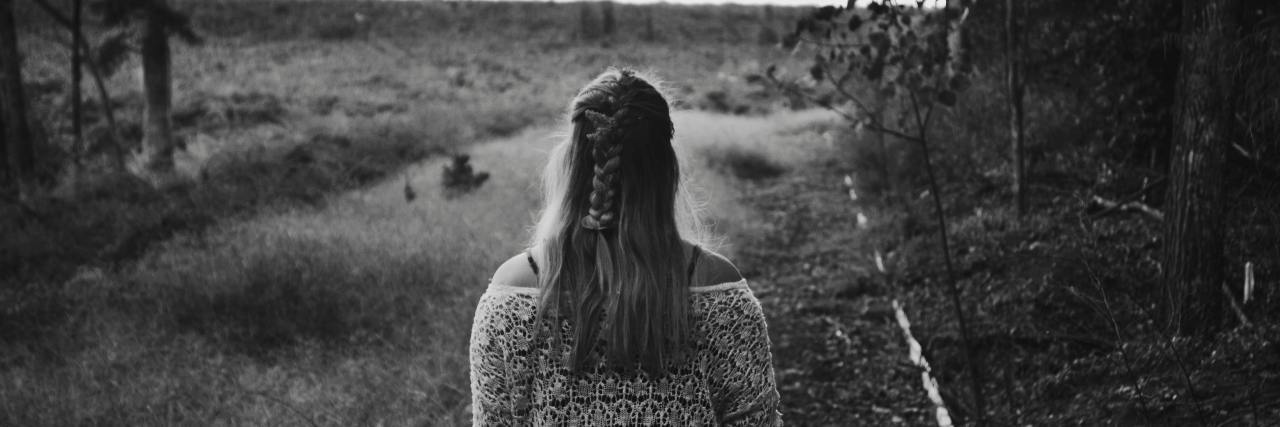 Black and white photo of the back of a woman in a dress walking on a trail