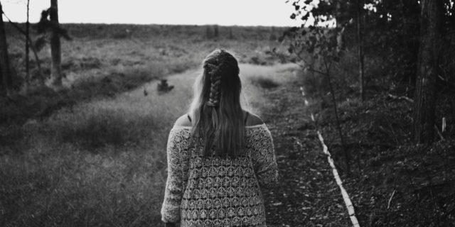 Black and white photo of the back of a woman in a dress walking on a trail