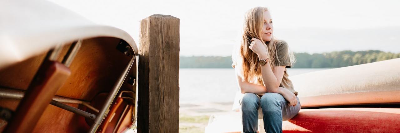 My Mental Health Journey Following Endometriosis Surgery Woman sitting on edge of boat on land by a dock and water, looking off to the side