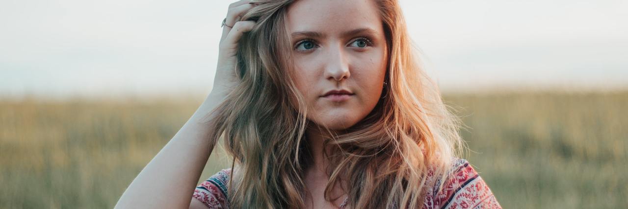 I Wish My Parents Knew I Had ADHD Growing Up photo of a woman in a field with her hand in her hair, looking off into distance