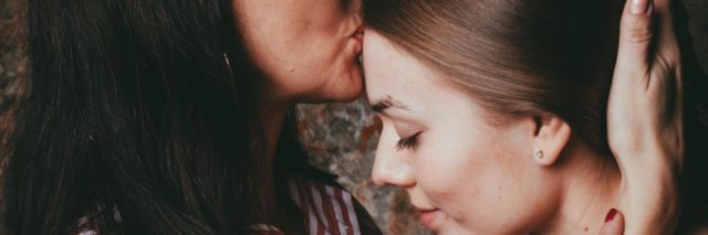 Mother giving grown daughter kiss on her forehead