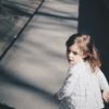 Little girl with brown hair looking behind while running down the sidewalk