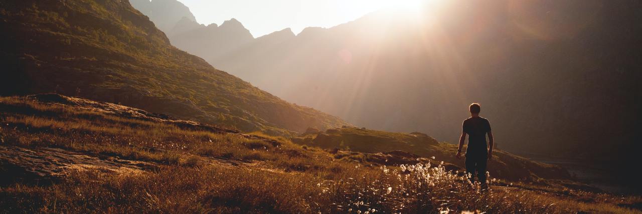 How Nature Can Be a Form of Self-Care for Mental Health photo of a man standing among mountains with sun setting