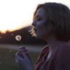 Profile of woman holding a dandelion and blowing it into the wind