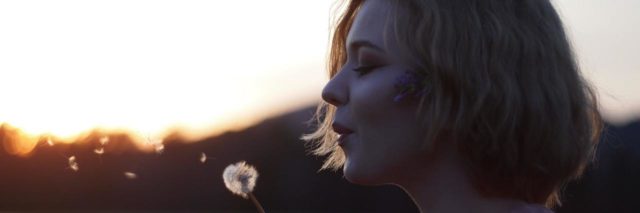 Profile of woman holding a dandelion and blowing it into the wind