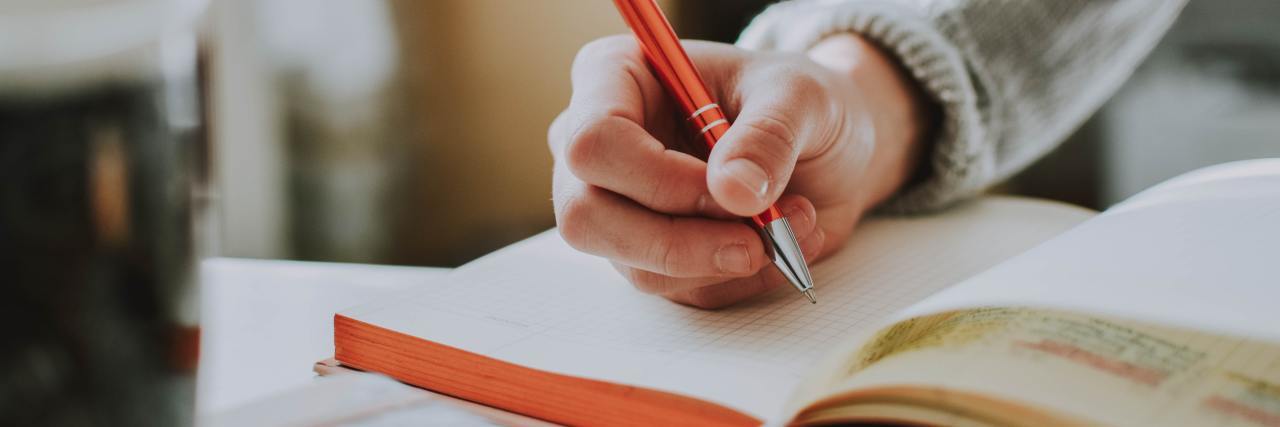 close up photo of a person's hand holding a pen and writing in a journal