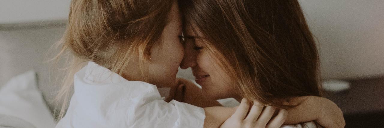 photo of a mother and daughter playing and hugging on a bed
