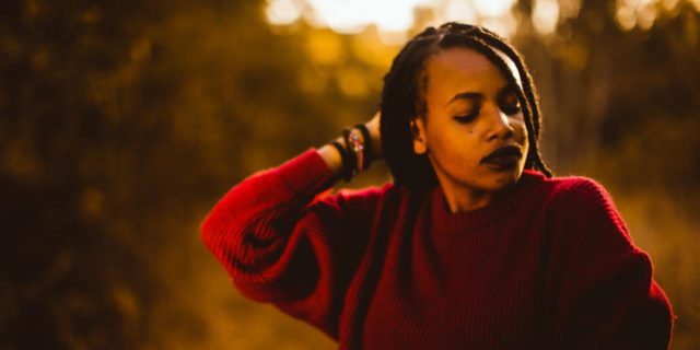 Why Calling Me a ‘Strong Black Woman’ Is Compromising My Mental Health photo of a woman at sunset with her eyes clsoed, hand raised to the back of her head