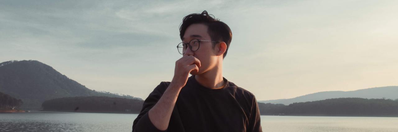 I Hate When ADHD Makes Me Talk Too Much photo of an asian man standing in front of a lake with his hand covering his mouth