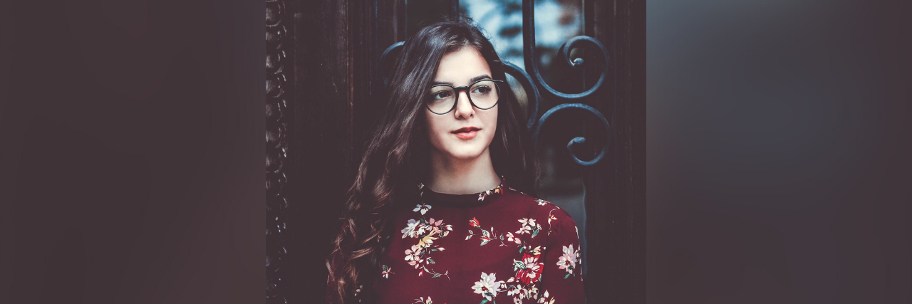 Choosing Self-Love Over Grandiosity in Bipolar Disorder Treatment Woman wearing glasses standing in front of wrought iron door