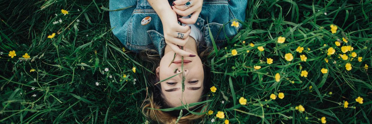A Letter to Both Those Diagnosed and Undiagnosed With OCD Young woman lying in a field with yellow flowers