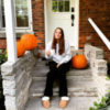 Photo of contributor sitting on front porch steps holding coffee mug, surrounded by three pumpkins