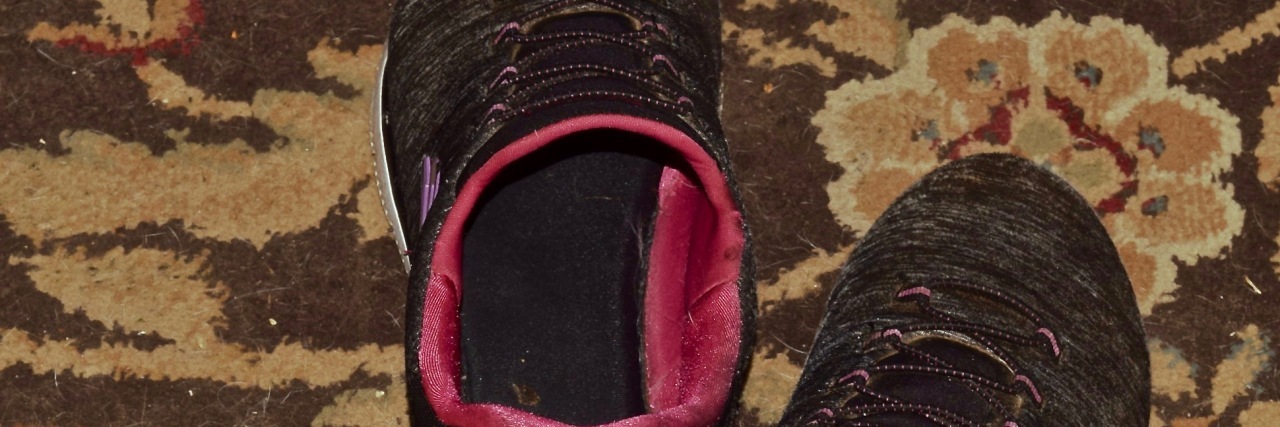 A pair of black and pink tennis shoes on a rug.