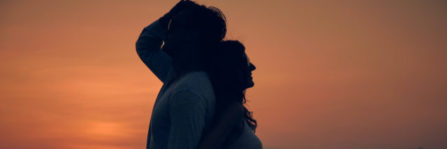 Silhouette of two people back to back at sunset