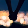Silhouette of cuple holding hands against blurred city night lights.