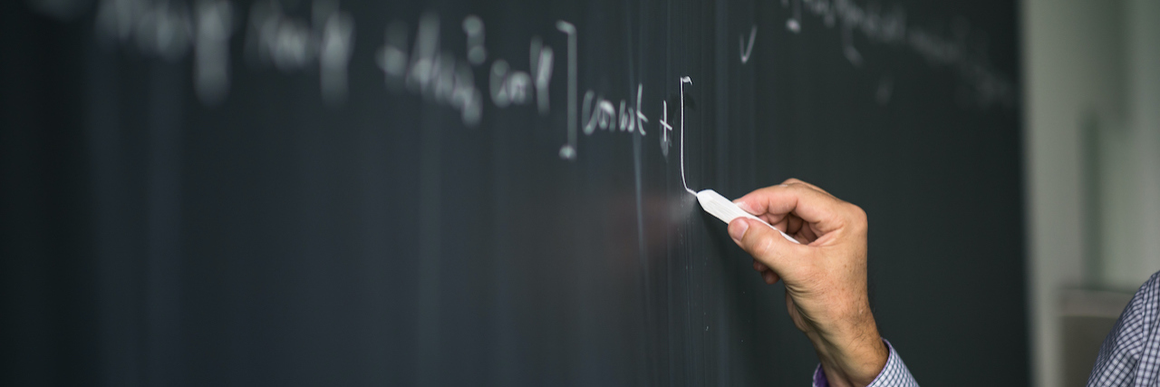 Mental Health and University: Why College Applications Are Ableist Math teacher by the blackboard during mathclass - detail of the hand with chalk