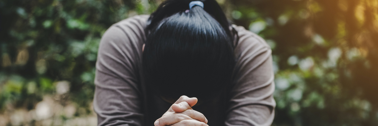 Woman with hands folded in prayer and head bowed, over a table with Bible on it