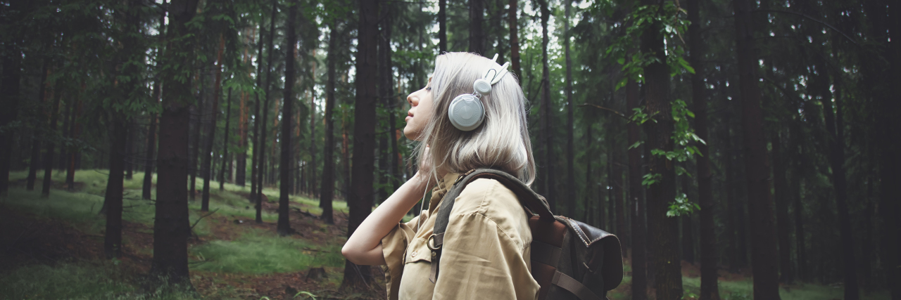 Why It’s OK, Even Necessary to Self-Diagnose in the Autism Community Blonde woman in headphones with backpack on rainy day in forest.