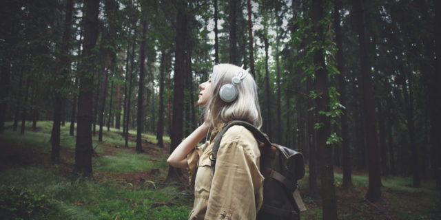 Blonde woman in headphones with backpack on rainy day in forest.