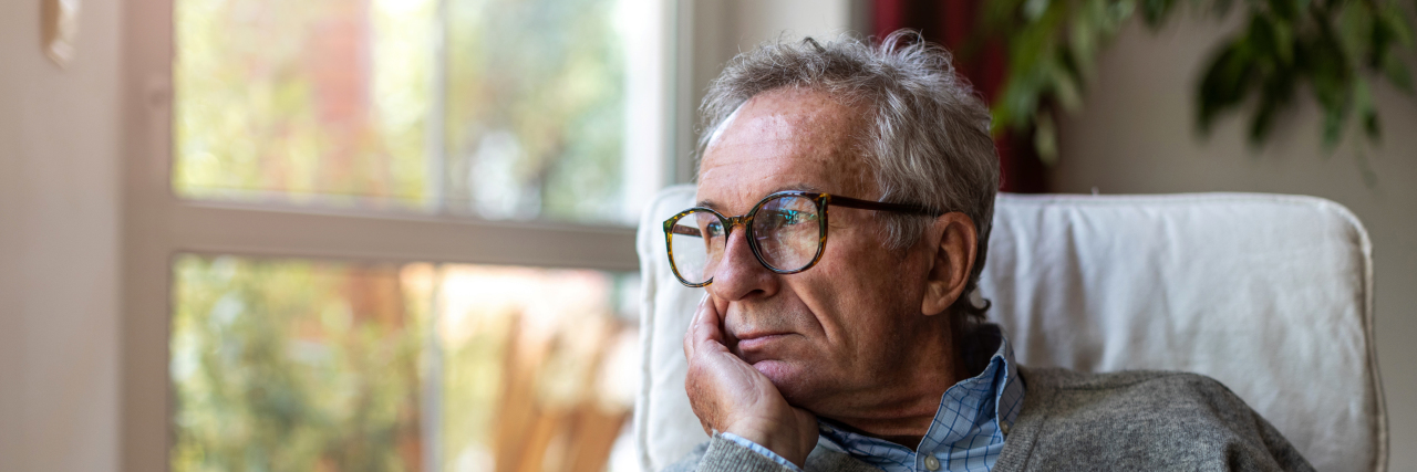 Why Is It Hard to Love Our Autistic Selves? Older man looking out of window at home.