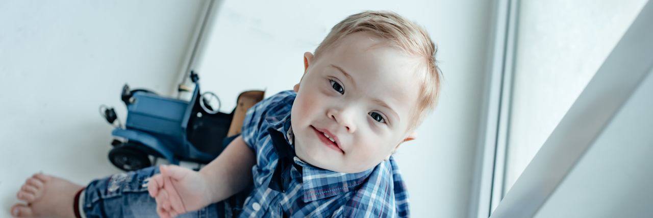 When Parenting a Child With Down Syndrome Is Hard A little boy in a plaid shirt with Down Syndrome plays with a toy truck.