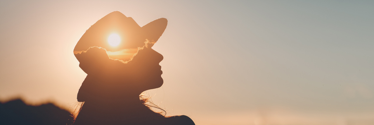 Yes, You Are 'Disabled Enough' Woman wearing a hat outdoors at sunset.