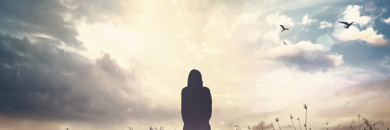 Silhouette of woman over autumn sunset meadow.