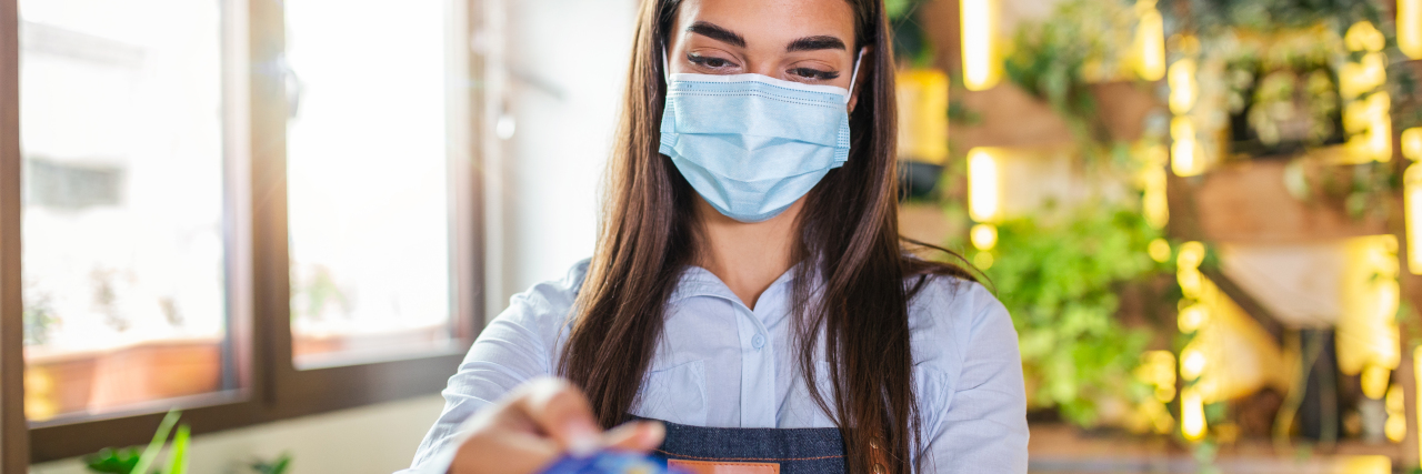 I'm Sick of Rude Responses When I Can't Hear Someone Wearing a Mask Waitress holding credit card reader machine and wearing protective face mask.