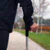 Man walking with a crutch outdoors on autumn day.