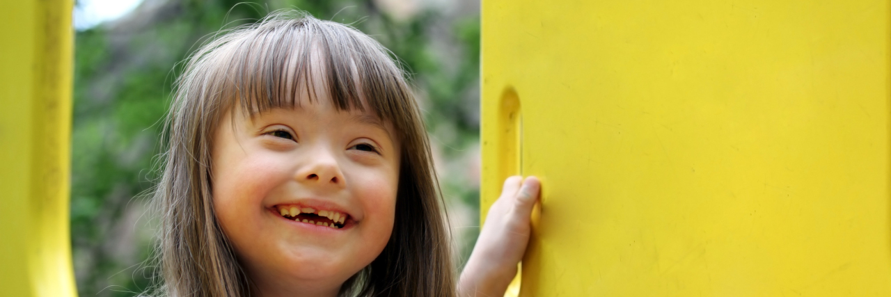 Should You Say 'Special Needs' or 'Disability?' Girl with Down syndrome on a playground.