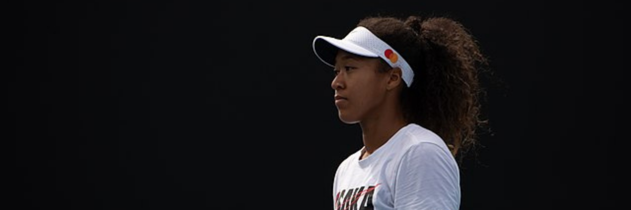 Naomi Osaka standing on tennis court waiting to receive the serve