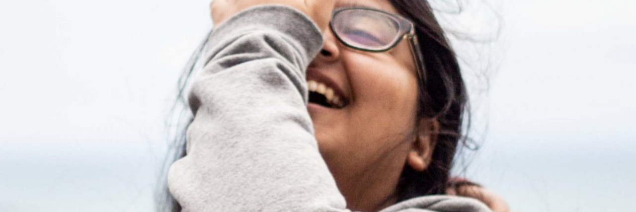 Why I Struggle Around My Suicide Attempt Anniversary Without Realizing photo of the contributor laughing with their eyes closed, hand partially covering face