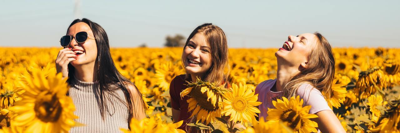photo of three women in a field of sunflowers, laughing