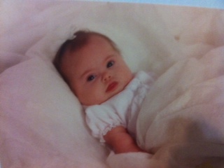 a babygirl wearing a white gown laying on a white bed