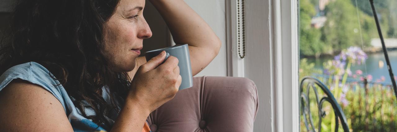 Reframing My Flight Response Helped My Complex PTSD photo of a woman sitting by a window drinking coffee