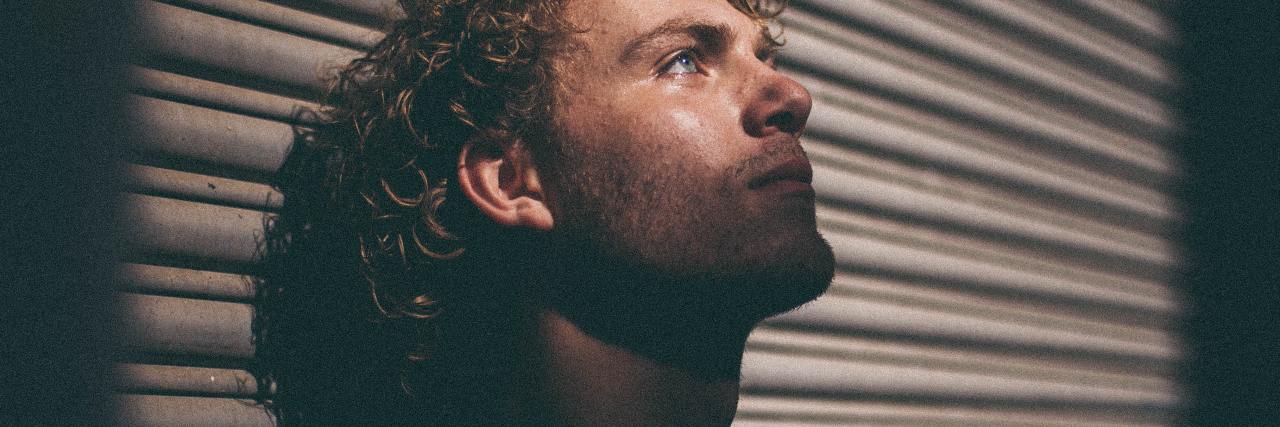 The Pressure to Feel ‘Fine’ With Bipolar Disorder photo of a man leaning back on a shutter, head raised, looking upset