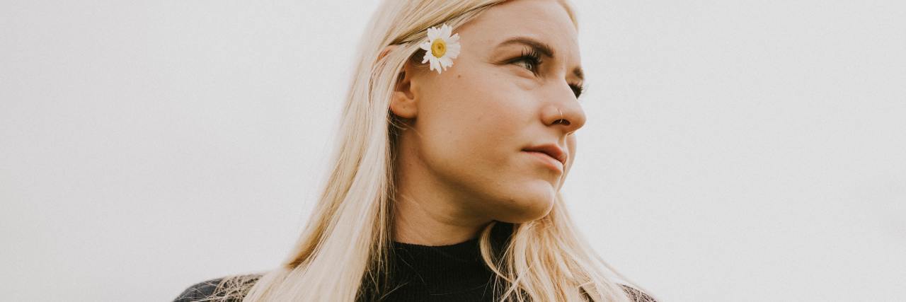 photo of a woman looking off into distance with a daisy in her blonde hair