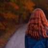 Back of a young woman walking outside during fall, long red hair
